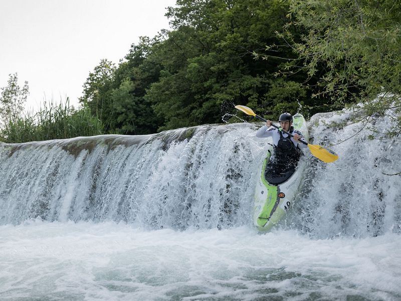 A person in a kayak goes over the edge of a short waterfall.