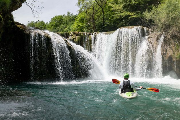 A kayaker floats in front of two short waterfalls.