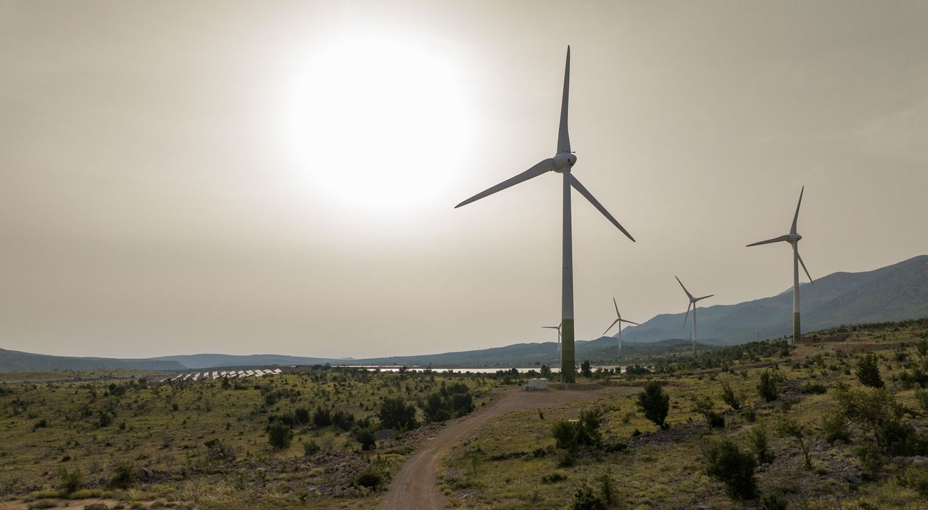 Aerial of several large wind turbines across a hilly landscape.