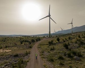 Aerial of several large wind turbines across a hilly landscape.