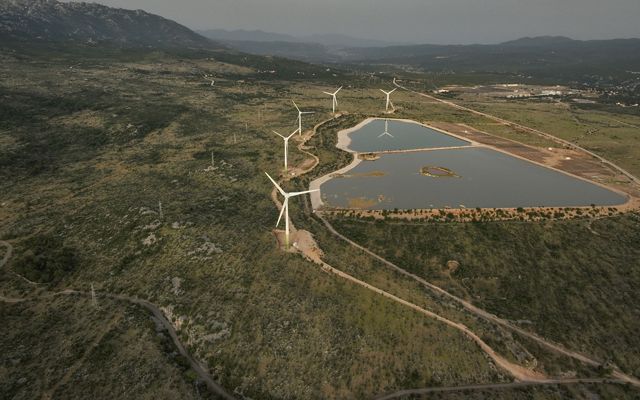 Aerial view of wind turbines at the edge of a manmade body of water at a power plant.