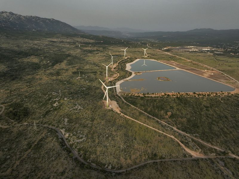 Aerial view of wind turbines at the edge of a manmade body of water at a power plant.