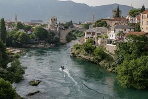 A town of stone with an arched bridge spans a river.