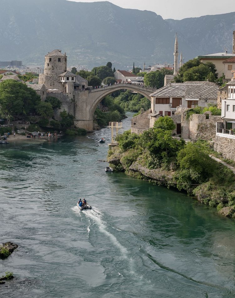 A town of stone with an arched bridge spans a river.