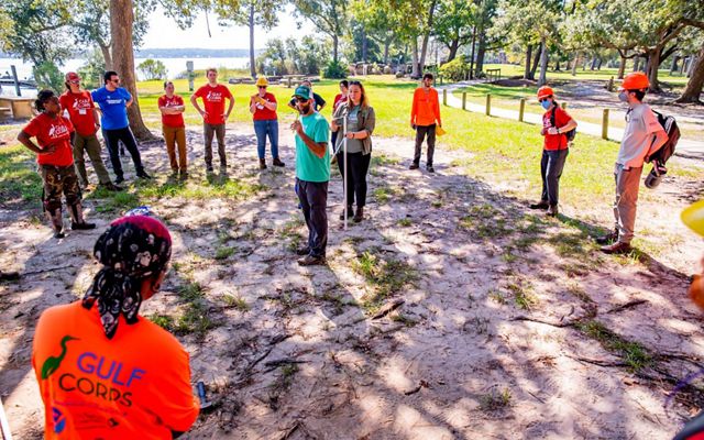 A group of people circle-up around a man and woman as the pair instruct the group on field-skills along Weeks Bay in Alabama.