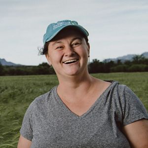 A woman wearing a grey shirt and a green hat smiles in a green field.