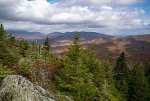 View from the top of Burnt Mountain shows a forested slope, then a valley and then distant mountains.