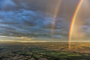 A double rainbow in front of a cloudy sky, with an ocean below. 