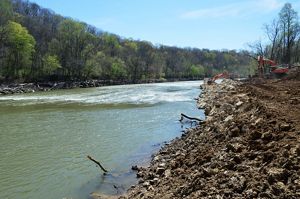 A river flows past loose rocks and digging equipment.
