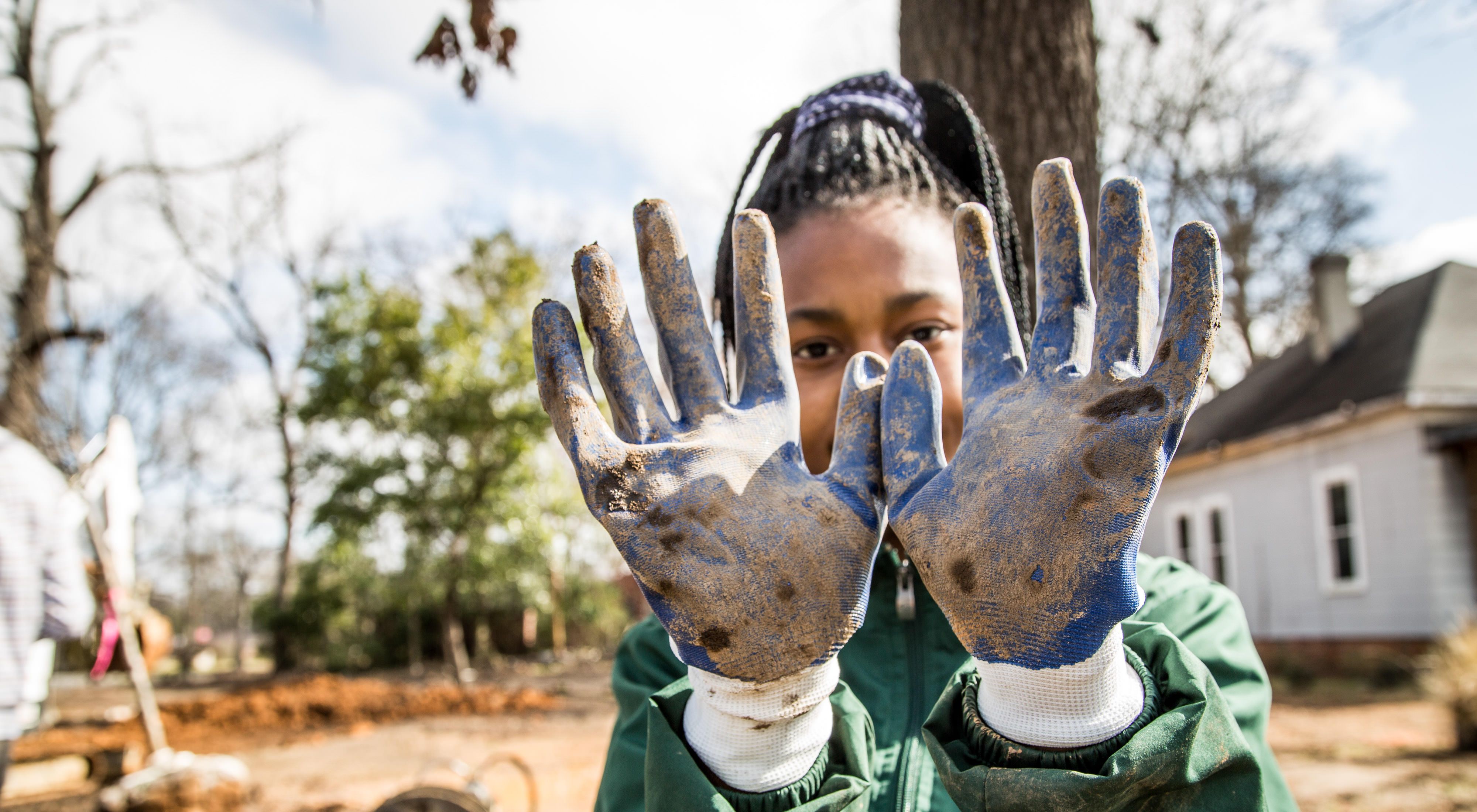 A young girl holds her gloved hands up to show off the dirt she got on them plantin trees