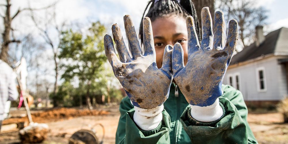 Una joven muestra sus guantes sucios de trabajar en el terreno.