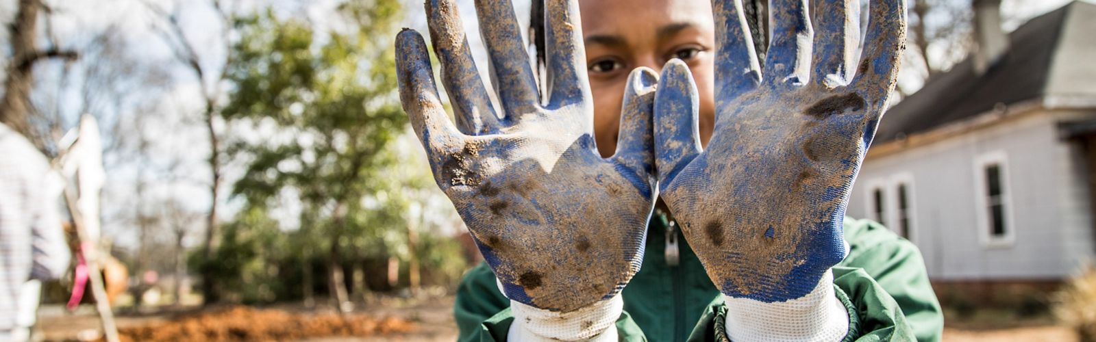 Una joven muestra sus guantes sucios de trabajar en el terreno.