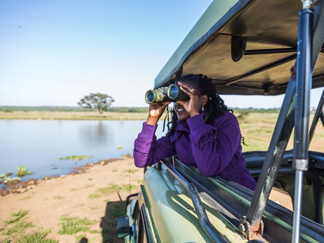 woman leaning out safari vehicle with binoculars