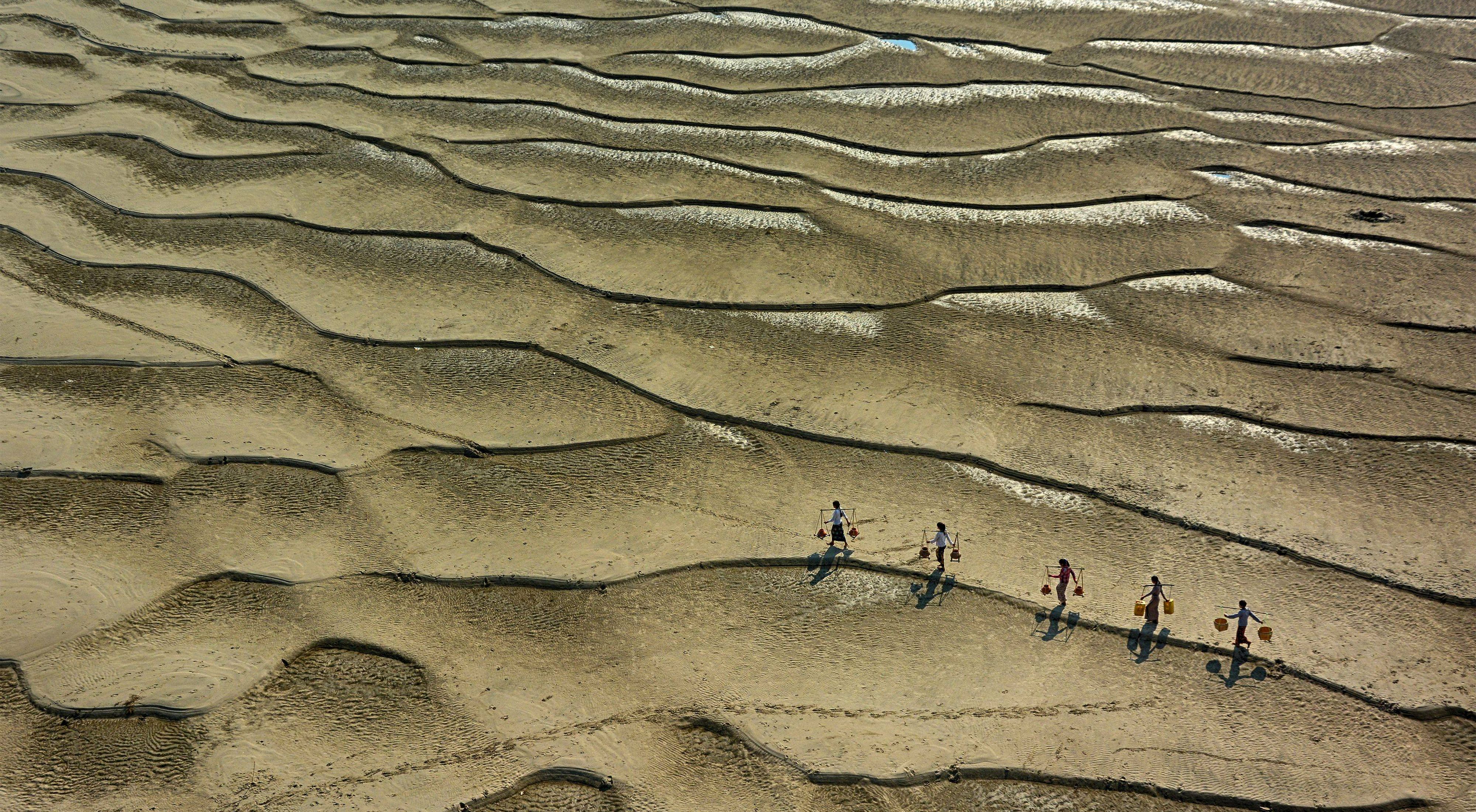 Aerial view of people carrying water in a riverbank.