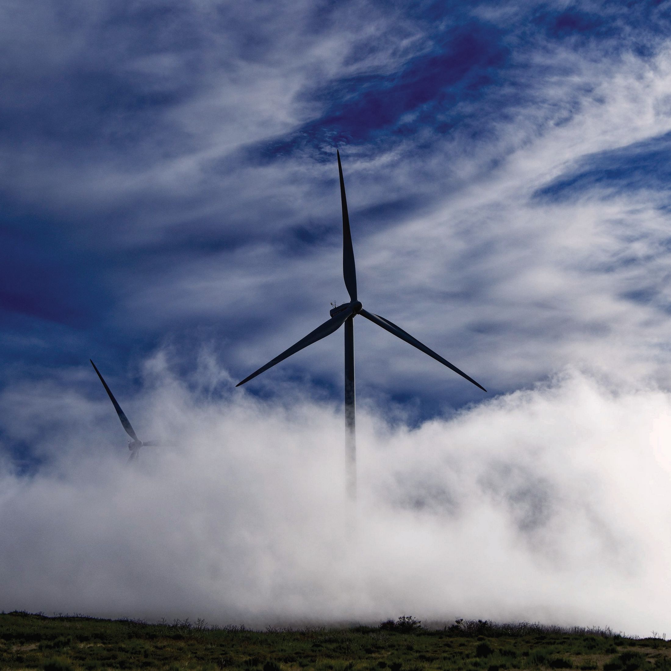 Photo of two wind turbines emerging from fog on the Paul da Serra plateau, Madeira, Portugal.