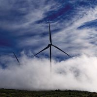 A wind turbine stands amid a foggy landscape.