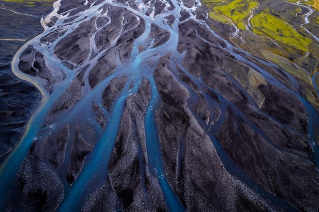 Aerial of several river channels weaving and crossing each other over black soil in Iceland