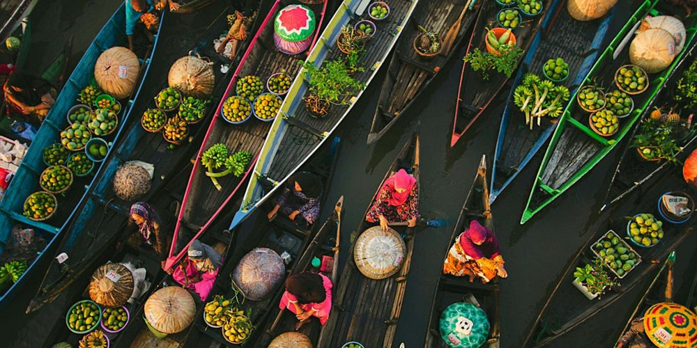 Aerial view of colorful boats transporting fruit and vegetables on a river.