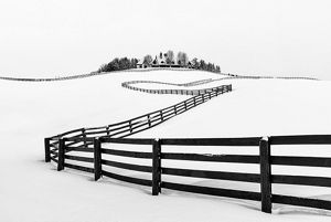 A fence winds and bends up a snow covered hill towards the house sitting atop it.