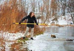 Brittney Rogers stands on the bank of the Salmon River on the lefthand side, using a yellow pole and bottle attached to it to collect a water sample. 