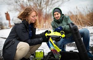 Brittney Rogers and Jacob Wojcik prepare a Remote Operated Vehicle (ROV) to collect media footage underwater. The tool is yellow and approximately handheld size.