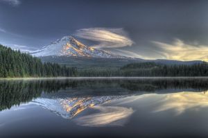 A scene of Mt. Hood, swept with feathery clouds, perfectly reflected in the lake below the mountain. 