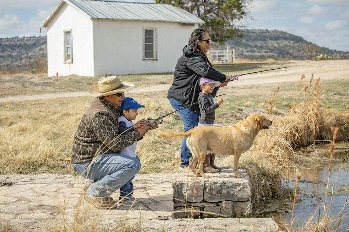 Man, woman and 2 children fish at the edge of a waterwater with arid land behind them