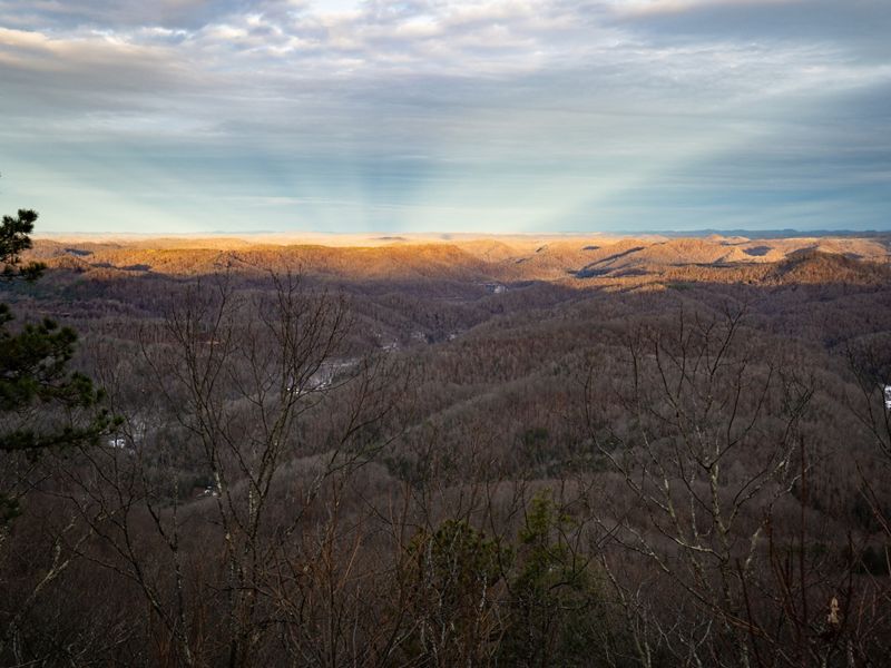 Distant mountain ridges that stretch to the horizon are bathed in golden sunlight. The landscape in the foreground is deep in shadow.