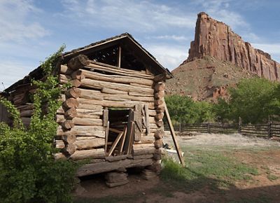 An old ranch building is dwarfed by red rock canyonland.
