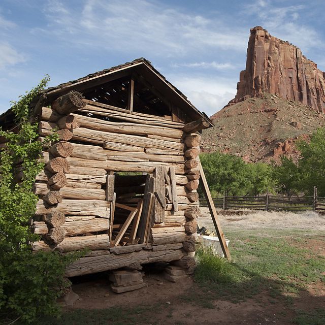An old ranch building is dwarfed by red rock canyonland.