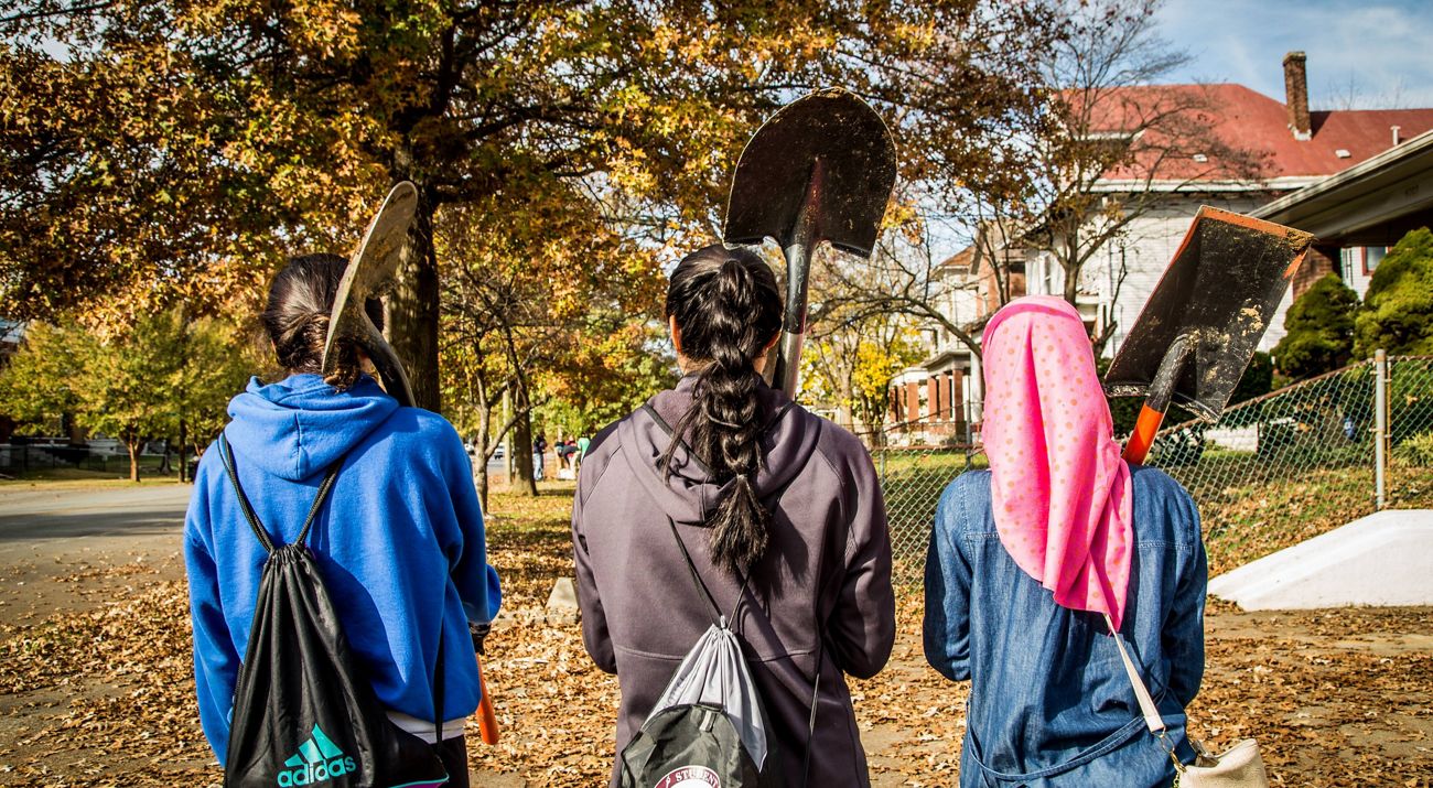 Three people holding shovels stand with their backs to the camera.