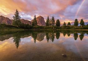 Sunset with rainbow over mountain lake.