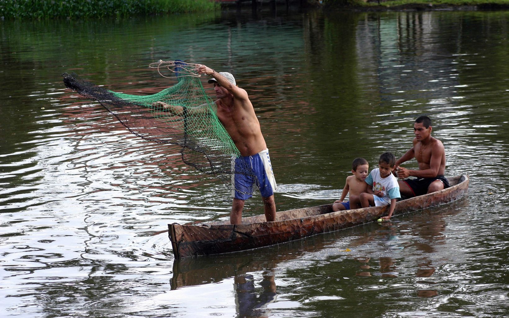 A family of Rama natives fish with a net from their boat on the San Juan River in tropical rainforest lowlands, Nicaragua. 