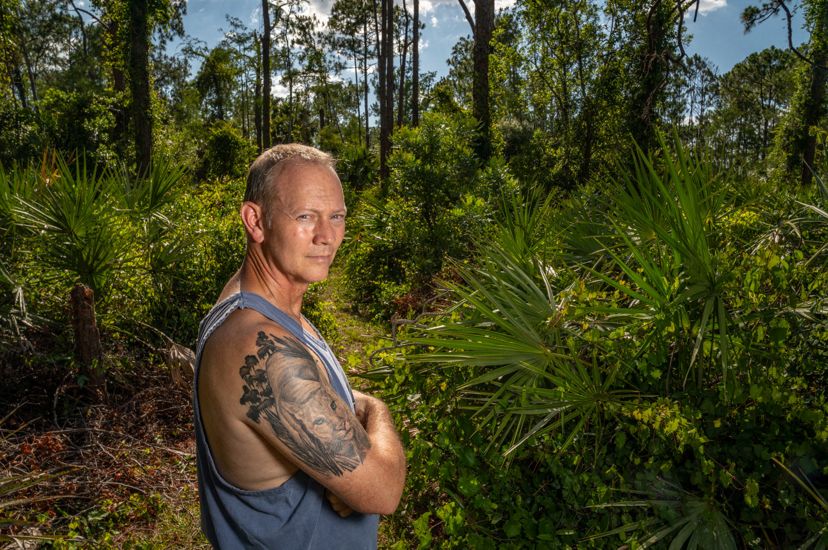 Florida man with tank top showing off florida panther tattoo on his arm while standing in a florida forest