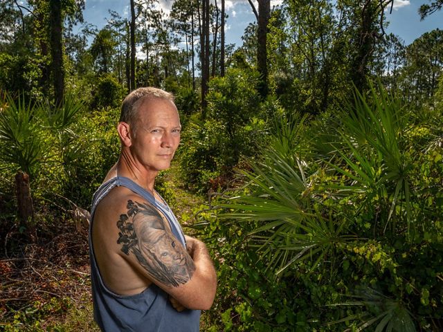 Florida man with tank top showing off florida panther tattoo on his arm while standing in a florida forest