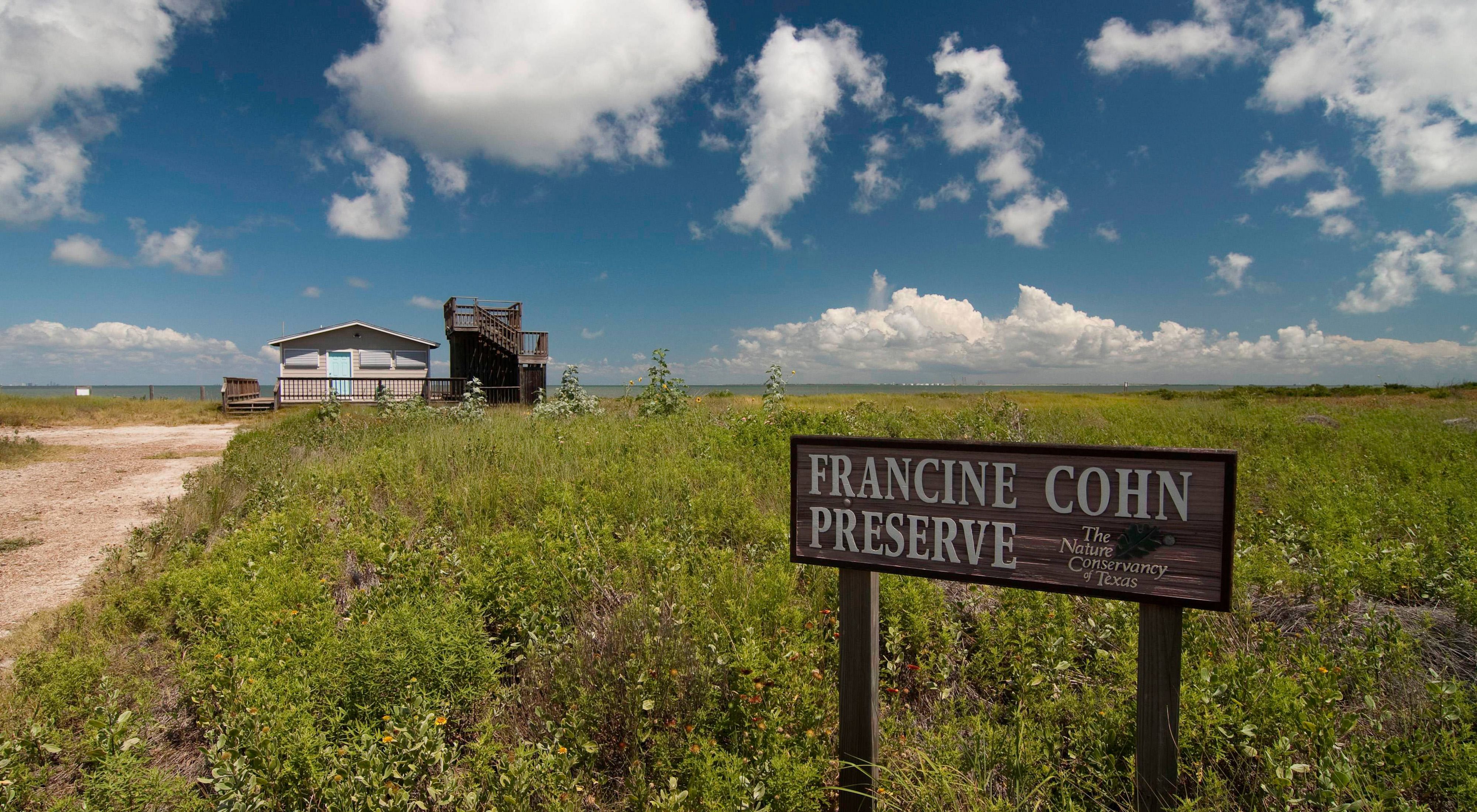 A sign reading the Francine Cohn Preserve, The Nature Conservancy of Texas, sits in front of a building along a beach. 