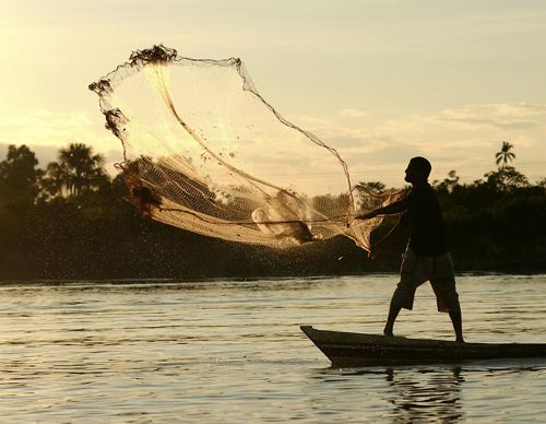 Pescador lanza su red de pesca sobre el rio Amazonas al atardecer.
