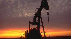 An oil rig is silhouetted against an orange sunset sky.