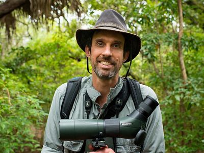 Portrait of a man standing in a forest, holding a monocular.
