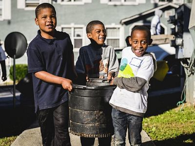 Three boys carry a black metal container during a volunteering activity.