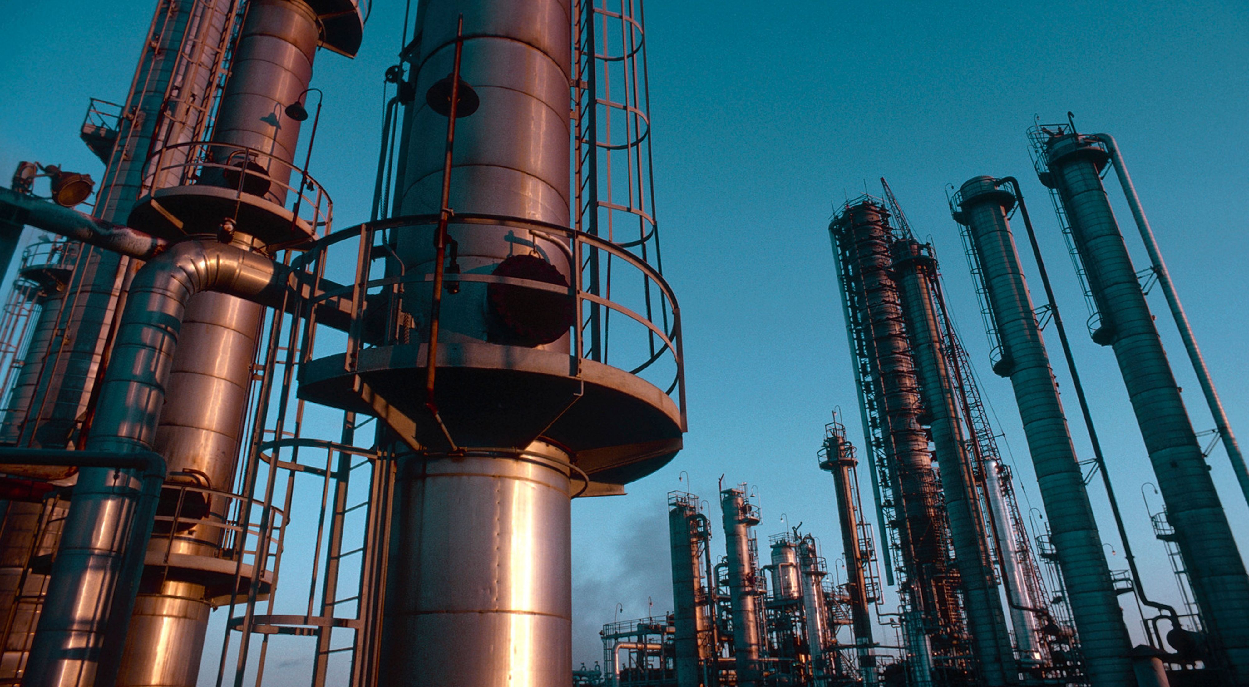 Photo of an oil refinery, with pipes and metal infrastructure.