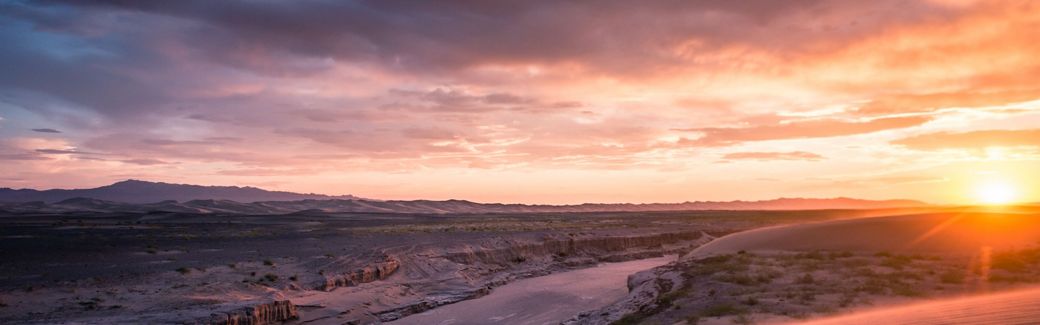 A river running through a landscape of canyons and the sun on the horizon.