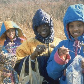 Three smiling youths in coats at a tree-planting event in Chicago.
