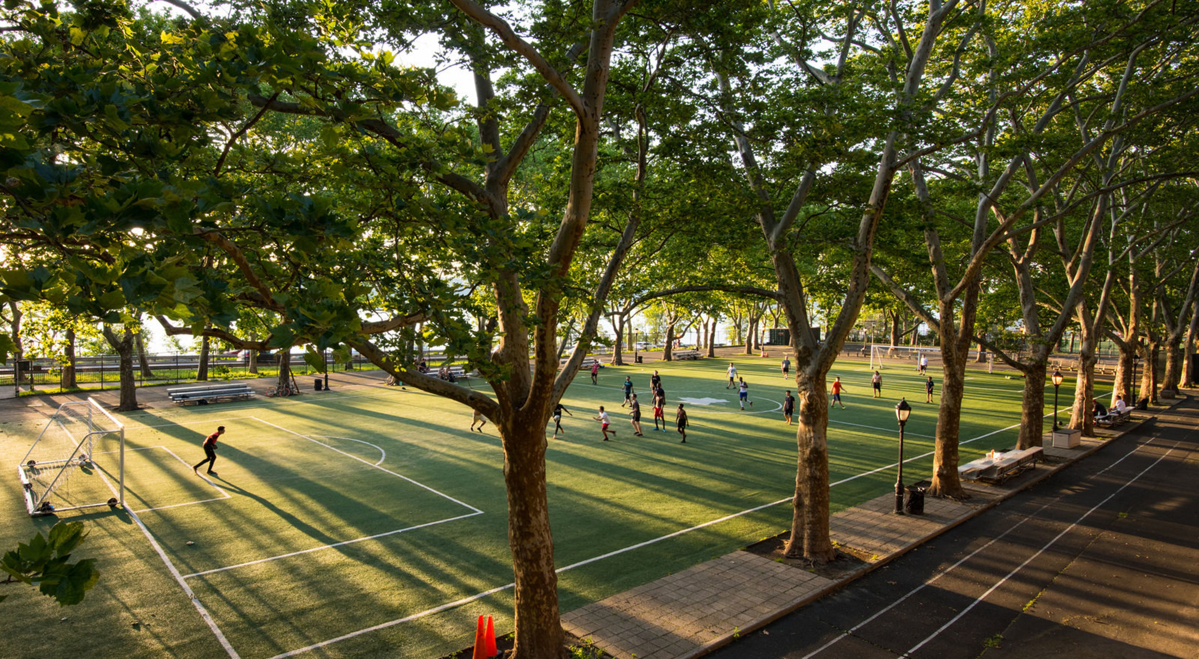 People play soccer on a field surrounded by large trees in New York City