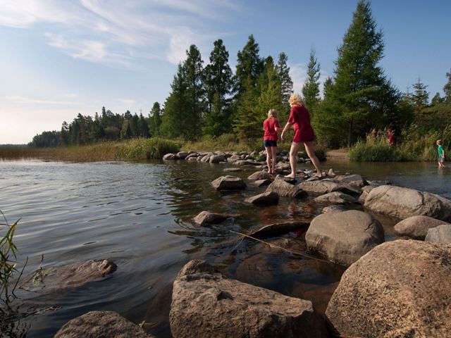 Two people in red shirts walk across big rocks that form a bridge across the Mississippi River with trees in the distance.