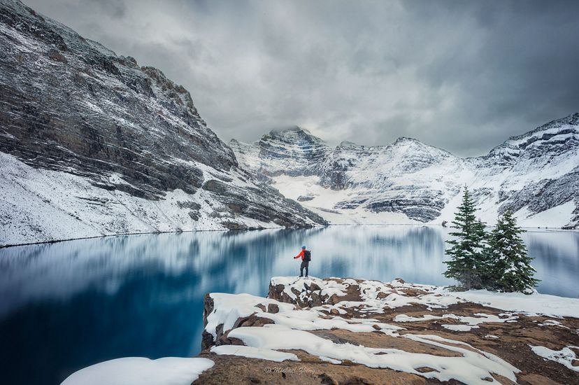 Senderista solitario junto a un lago de montañas nevadas.