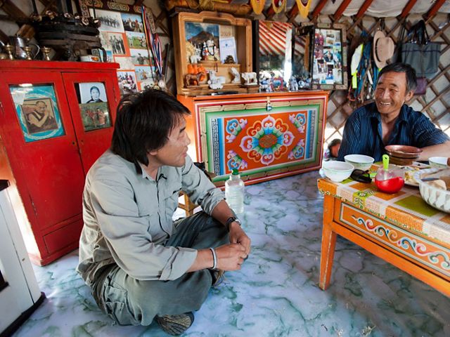 two men sit on the floor around a table in a yurt