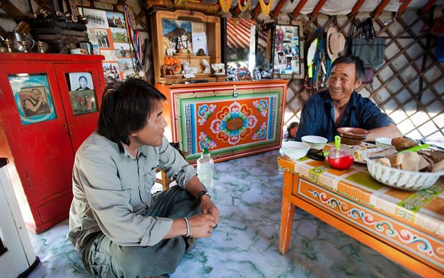 dos hombres se sientan en el suelo alrededor de una mesa en una yurta