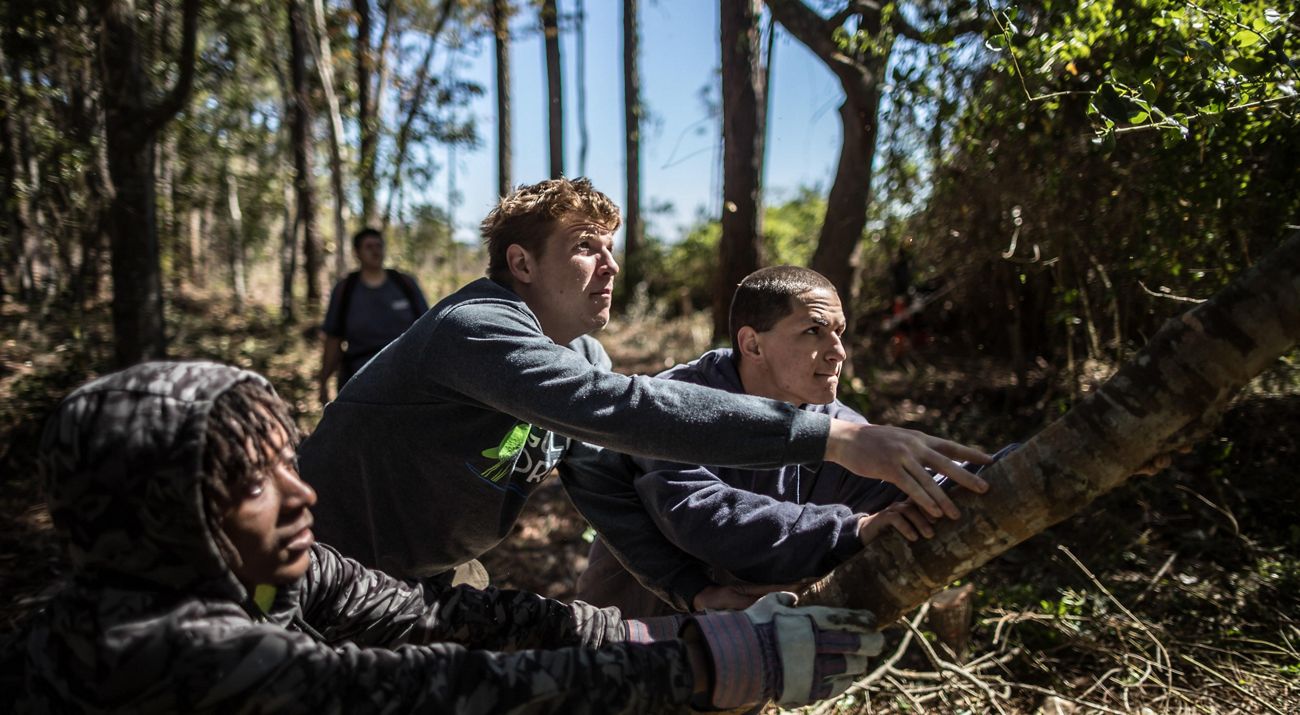 Three people work together to push a fallen tree away from a trail.