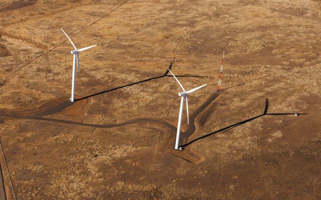 Two wind turbines are spinning on vast brown grasslands.